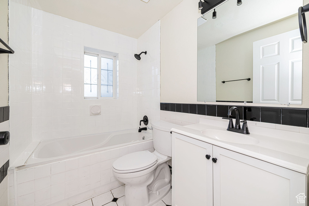 Full bathroom with vanity, toilet, tile walls, tile patterned floors, and tiled shower / bath combo
