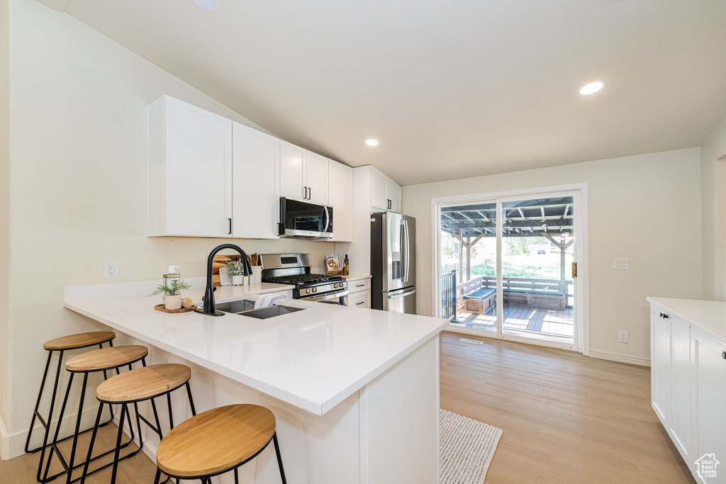 Kitchen featuring a breakfast bar, light countertops, a sink, light wood-style flooring, and appliances with stainless steel finishes