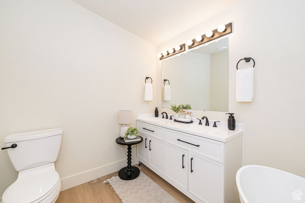 Full bathroom with double vanity, a freestanding bath, wood finished floors, a sink, and toilet