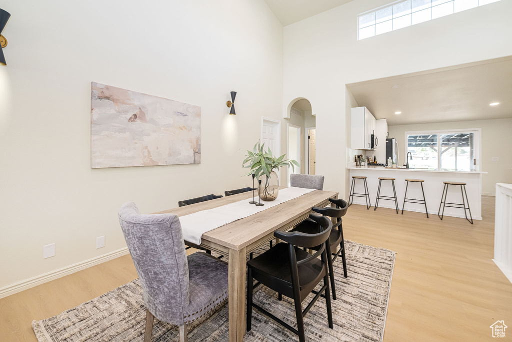 Dining room featuring a high ceiling, arched walkways, recessed lighting, baseboards, and light wood-type flooring