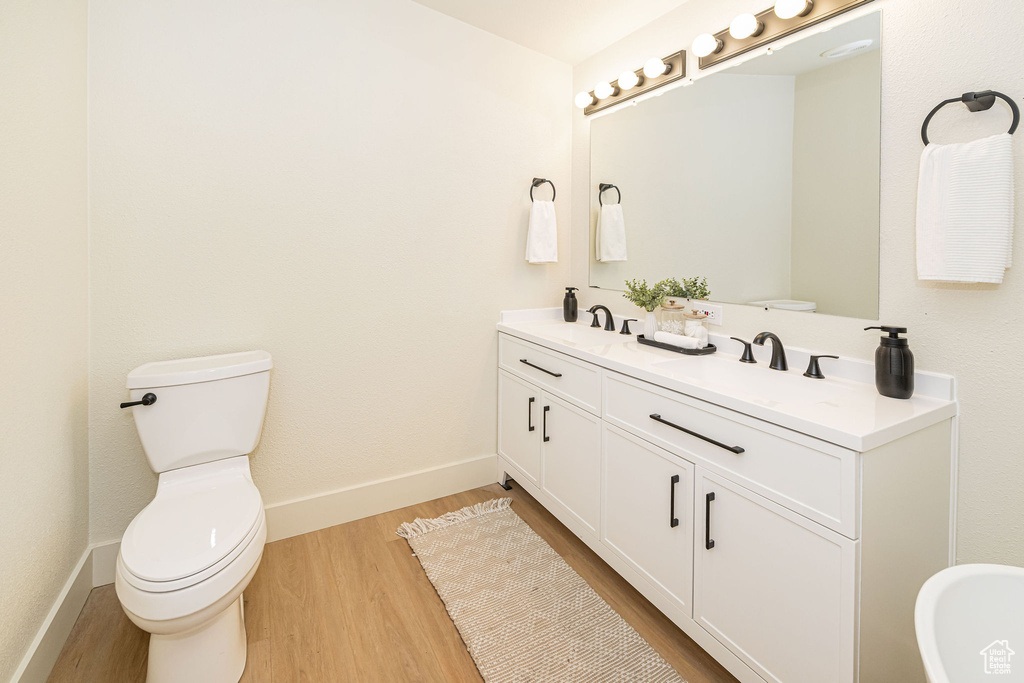 Bathroom with a sink, double vanity, toilet, baseboards, and wood finished floors