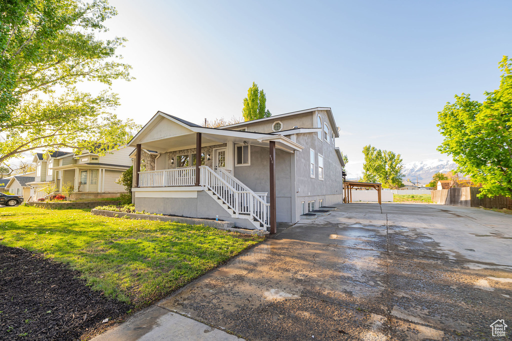 View of front of home with covered porch, a carport, a front lawn, concrete driveway, and stairs