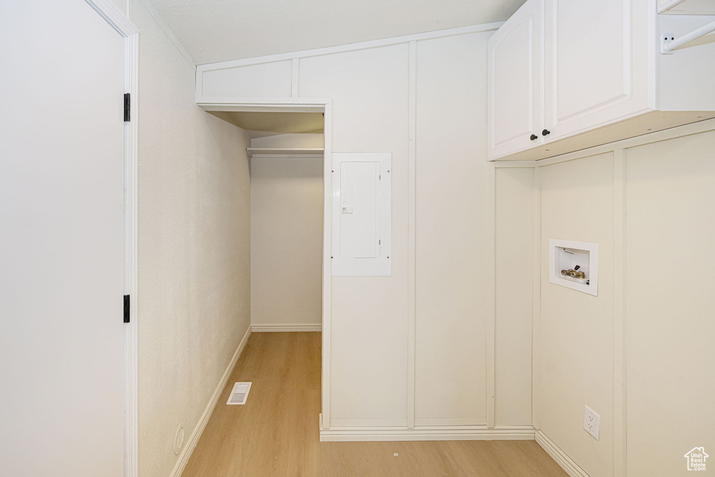 Clothes washing area with washer hookup, electric panel, visible vents, cabinet space, and light wood-style floors