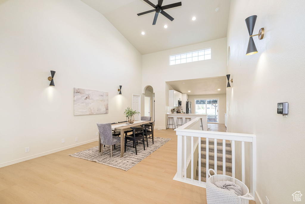 Dining room with arched walkways, a ceiling fan, light wood-type flooring, and high vaulted ceiling