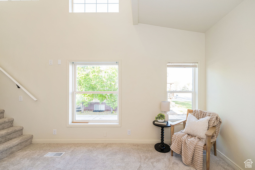 Living area with carpet floors, high vaulted ceiling, a healthy amount of sunlight, visible vents, and stairway