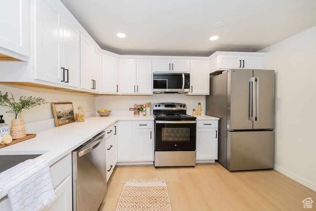 Kitchen with light countertops, light wood-style flooring, appliances with stainless steel finishes, and white cabinets
