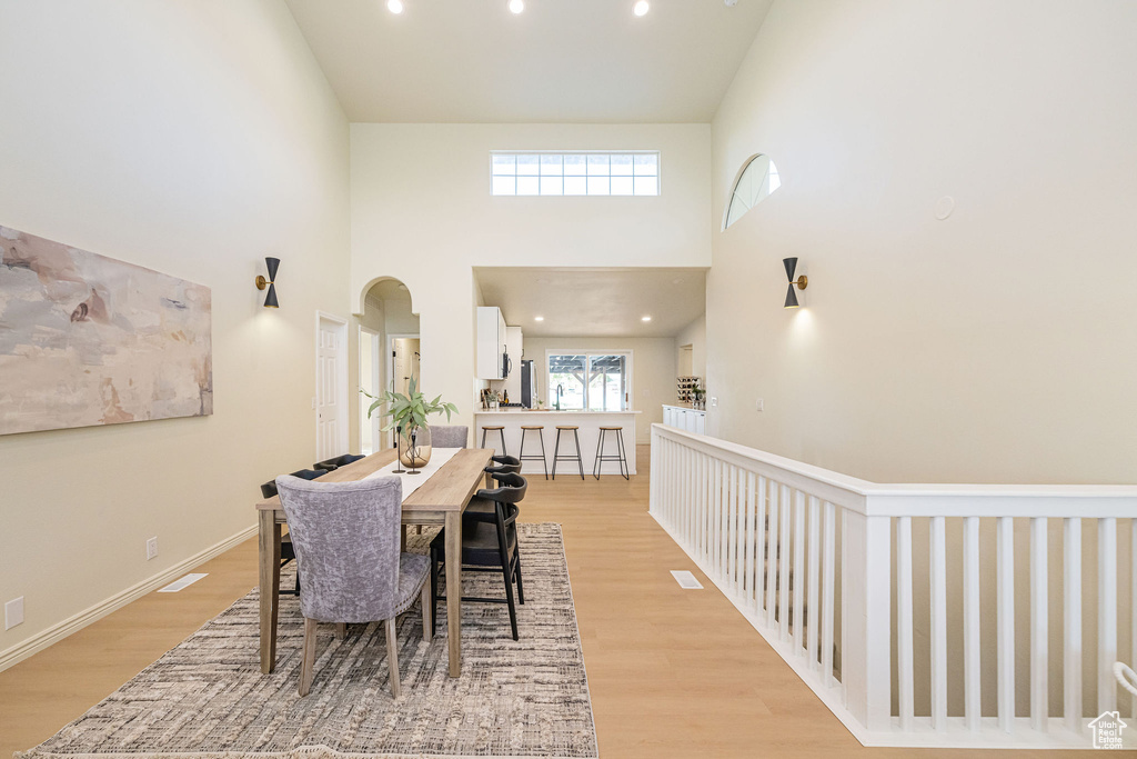 Dining area with recessed lighting, arched walkways, light wood-type flooring, and a towering ceiling