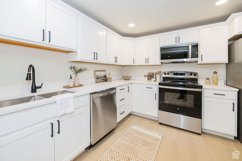 Kitchen featuring light countertops, white cabinetry, a sink, light wood finished floors, and appliances with stainless steel finishes