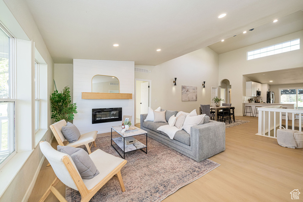 Living room with recessed lighting, arched walkways, a large fireplace, and light wood finished floors