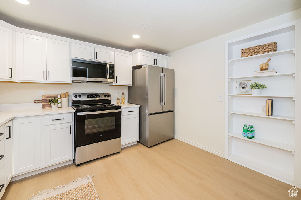 Kitchen featuring light wood-type flooring, light countertops, recessed lighting, white cabinets, and stainless steel appliances