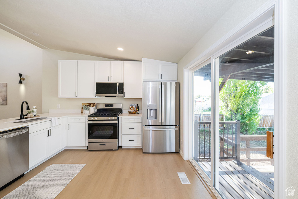 Kitchen with light wood finished floors, lofted ceiling, white cabinets, and stainless steel appliances