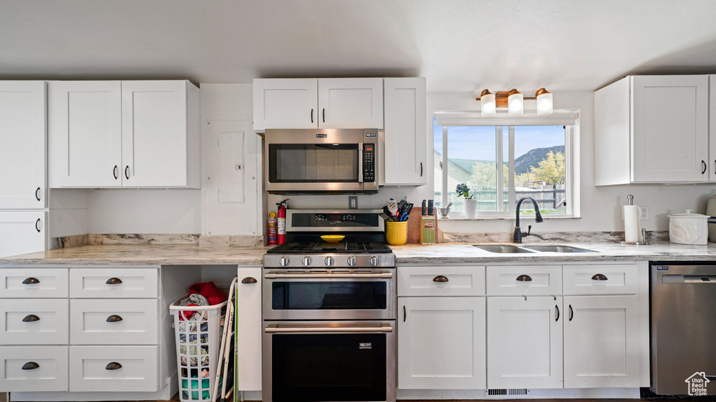 Kitchen with white cabinetry, light stone countertops, stainless steel appliances, and a sink