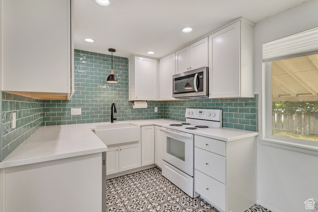 Kitchen with white cabinets, backsplash, stainless steel microwave, and electric stove