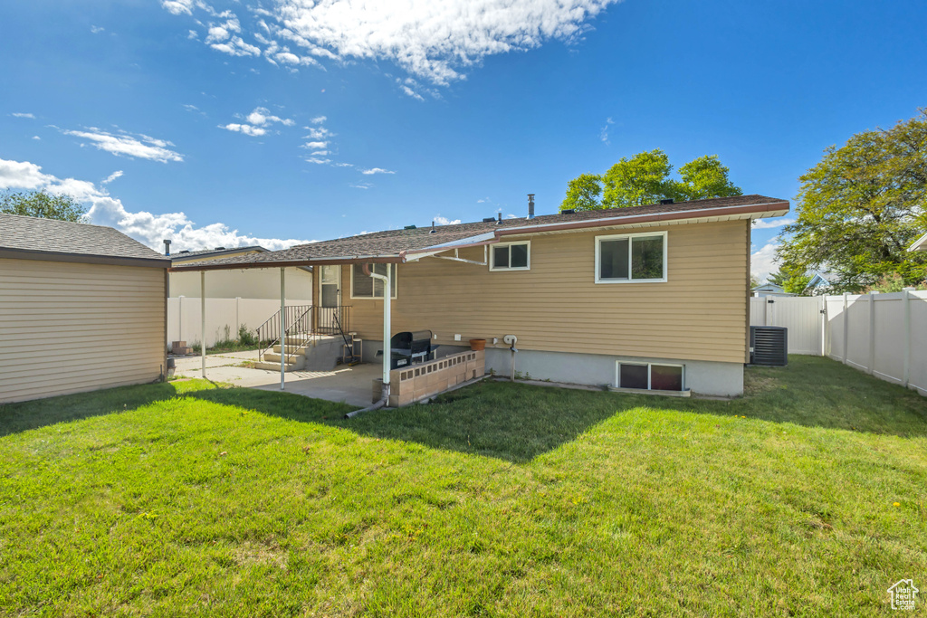 Rear view of house featuring a yard, cooling unit, a fenced backyard, and a patio area