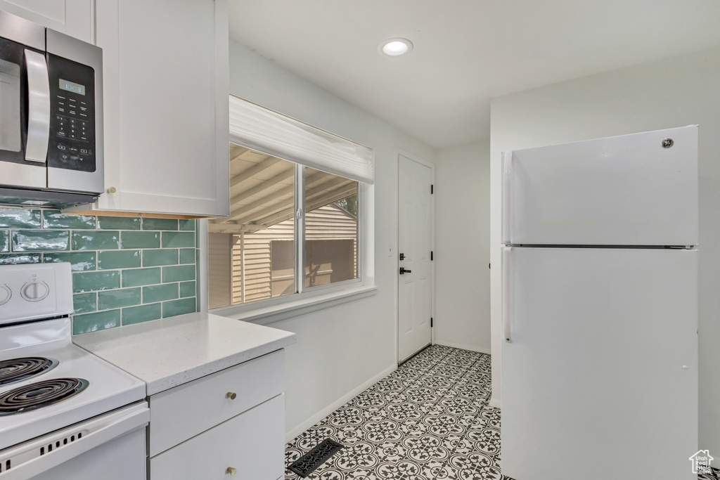 Kitchen featuring white cabinets, white appliances, light countertops, baseboards, and tasteful backsplash