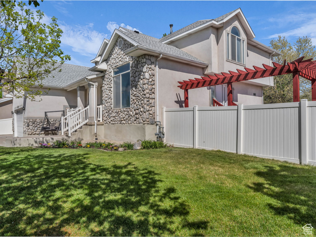 View of side of property featuring fence, a yard, a pergola, stone siding, and stucco siding