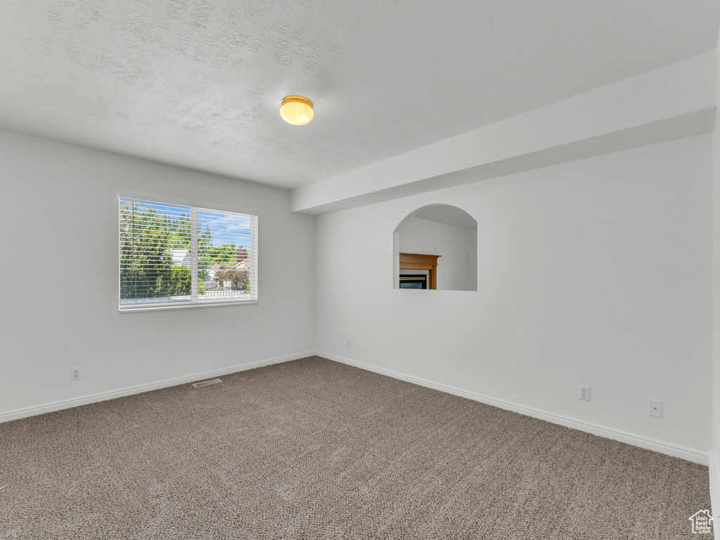 Carpeted spare room featuring baseboards, a textured ceiling, and visible vents