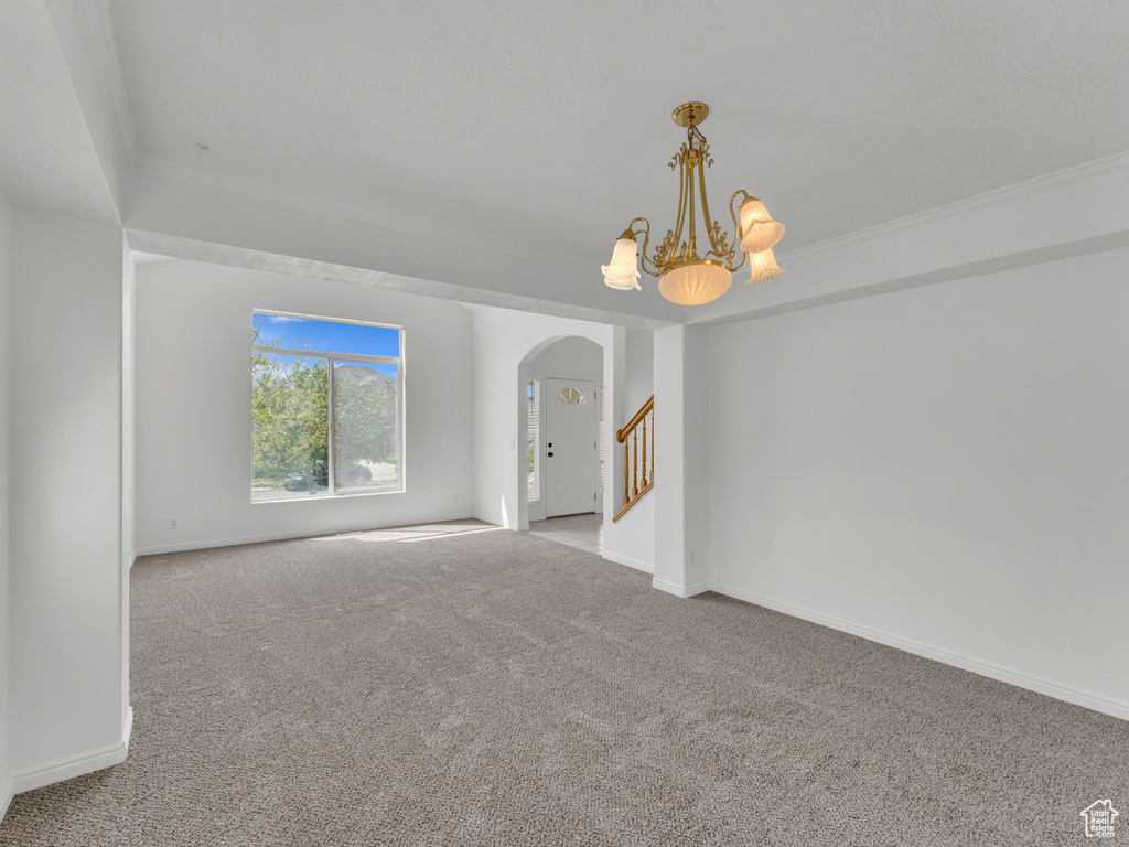 Carpeted spare room with arched walkways, baseboards, a notable chandelier, and stairway