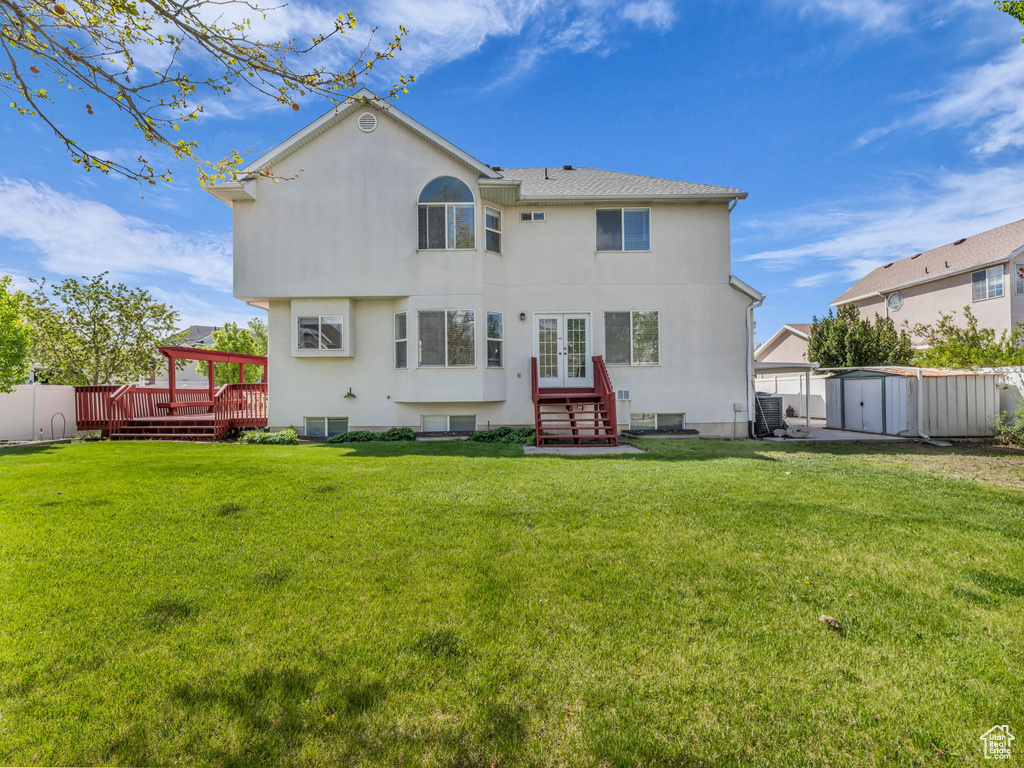 Rear view of property featuring an outdoor structure, a wooden deck, a shed, french doors, and a lawn