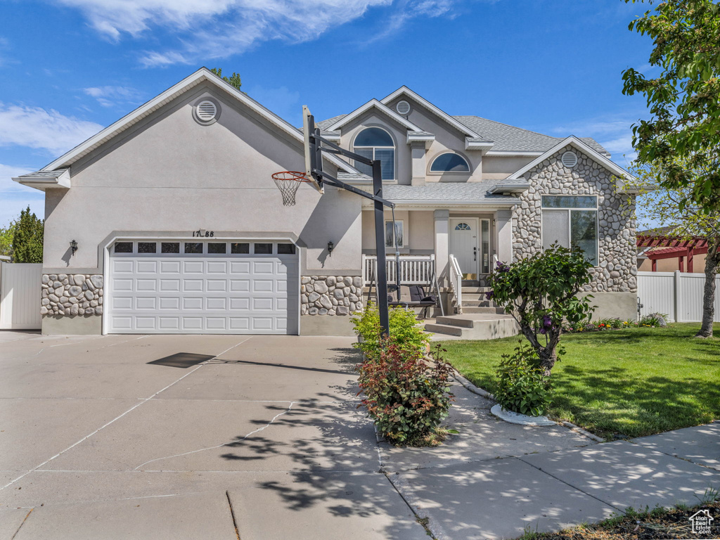 View of front of house with an attached garage, a front lawn, stone siding, stucco siding, and driveway
