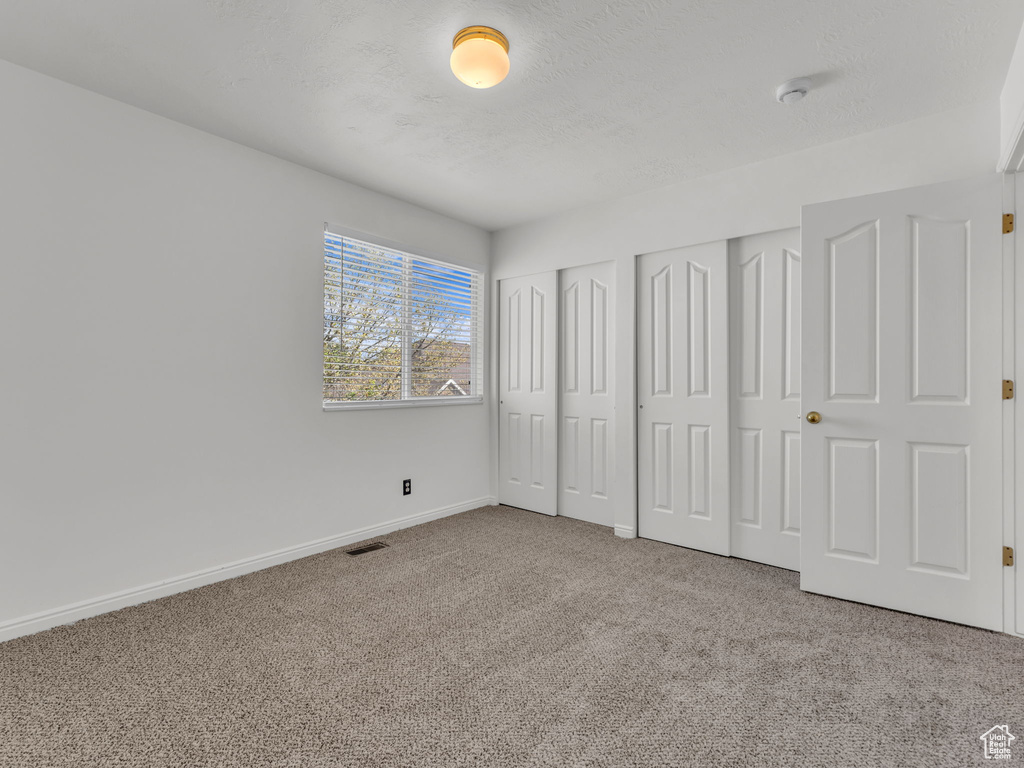 Unfurnished bedroom with two closets, carpet flooring, visible vents, and baseboards