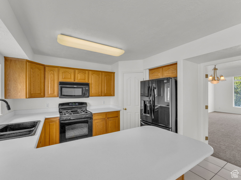Kitchen with a notable chandelier, light carpet, a sink, light countertops, and black appliances