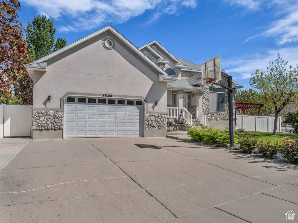 View of front of property with fence, an attached garage, stone siding, stucco siding, and driveway