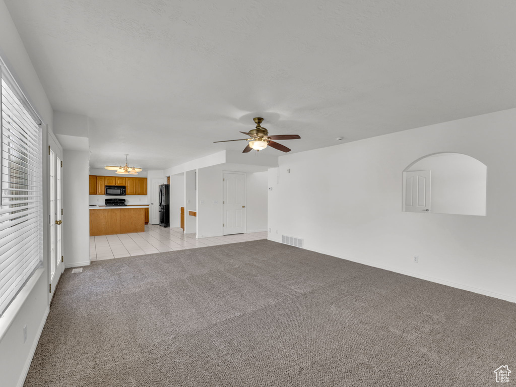 Unfurnished living room with baseboards, visible vents, light carpet, and ceiling fan with notable chandelier