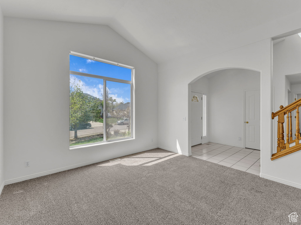 Spare room featuring lofted ceiling, light tile patterned flooring, baseboards, light colored carpet, and arched walkways