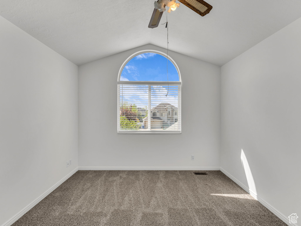 Spare room featuring ceiling fan, visible vents, vaulted ceiling, baseboards, and carpet flooring