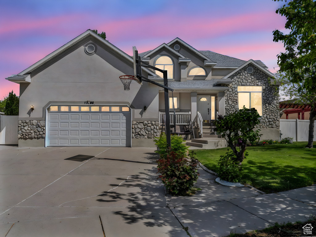 View of front of property with a front lawn, stone siding, stucco siding, concrete driveway, and an attached garage