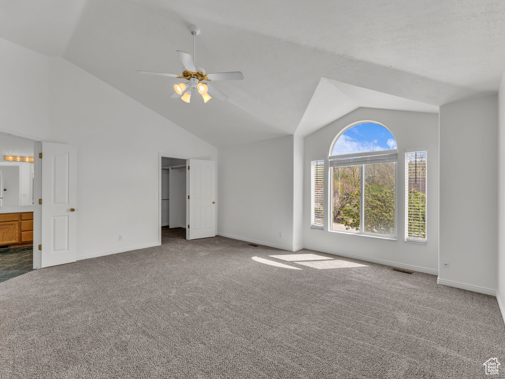 Unfurnished bedroom featuring visible vents, carpet floors, baseboards, high vaulted ceiling, and ensuite bathroom