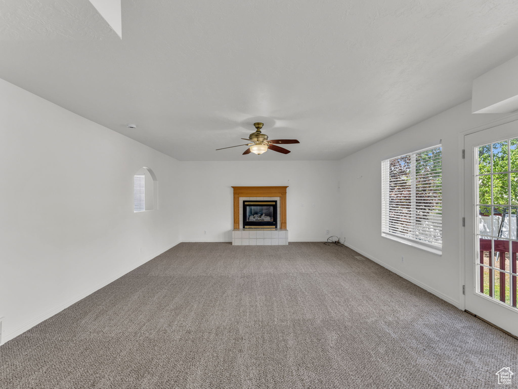 Unfurnished living room with baseboards, ceiling fan, carpet, and a tile fireplace