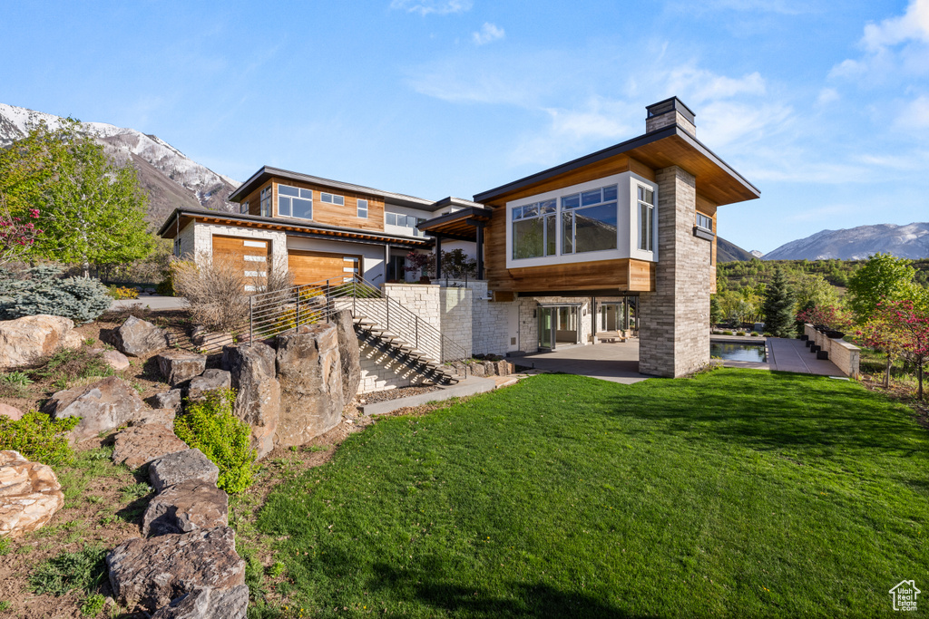 Back of house with stairway, a patio, a chimney, a lawn, and a mountain view