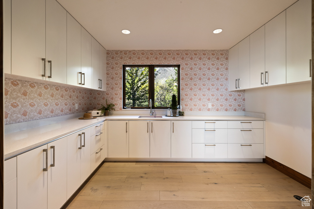 Kitchen with a sink, light wood-style floors, light countertops, tasteful backsplash, and white cabinetry