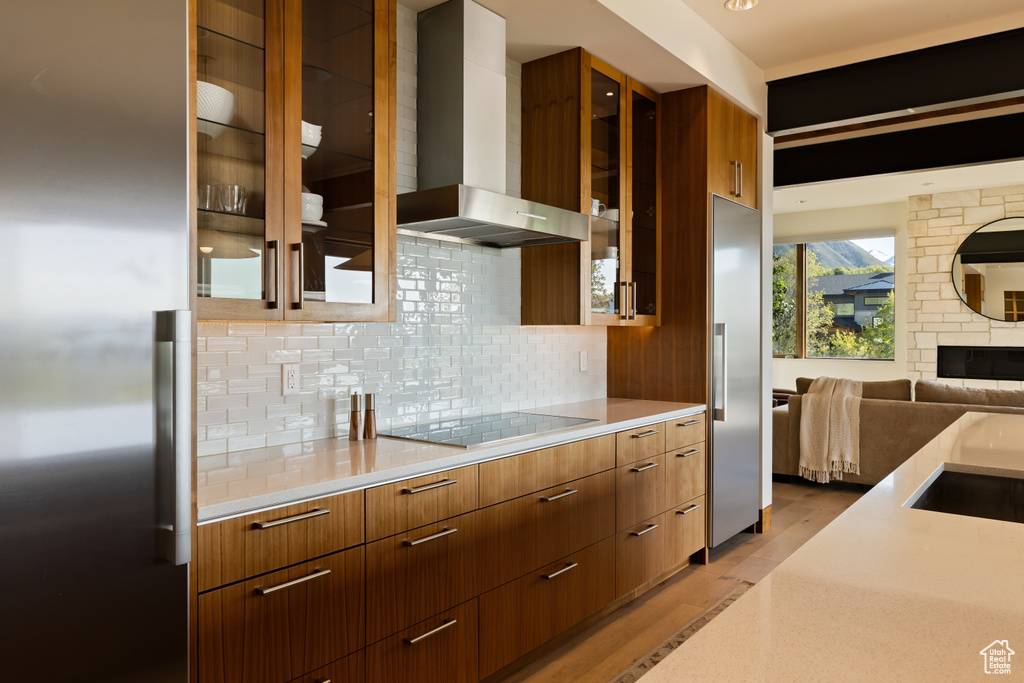 Kitchen with wall chimney range hood, black electric cooktop, modern cabinets, and built in refrigerator