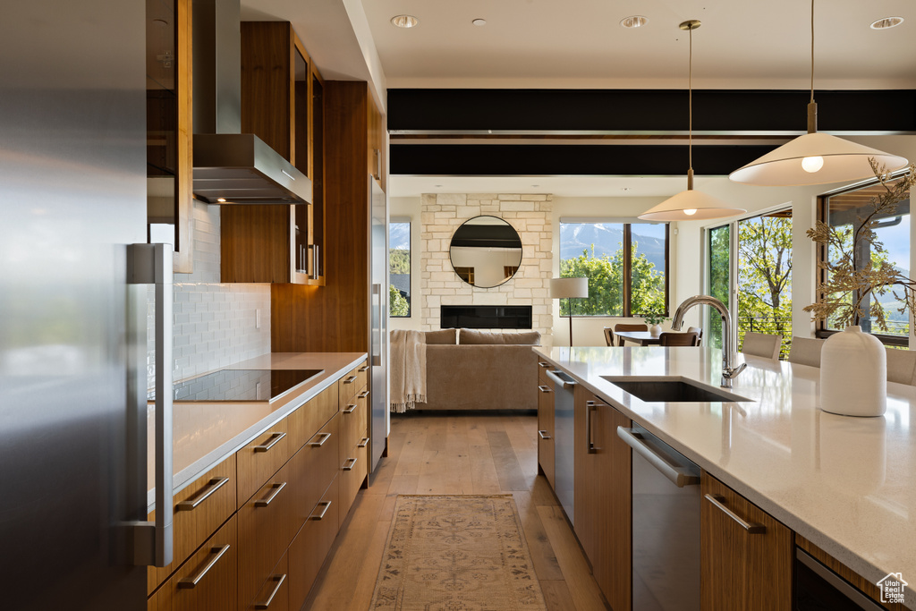 Kitchen featuring modern cabinets, a sink, stainless steel appliances, wall chimney exhaust hood, and brown cabinets