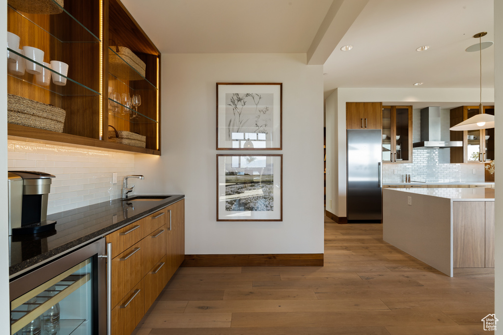 Bar featuring wall chimney exhaust hood, beverage cooler, stainless steel fridge, a sink, and baseboards