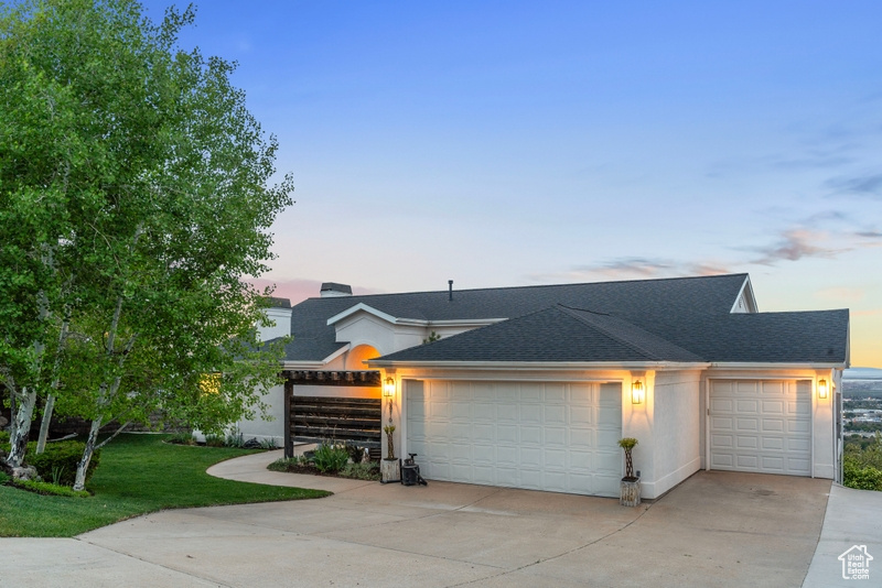 View of front of home with a garage, a yard, driveway, and a shingled roof