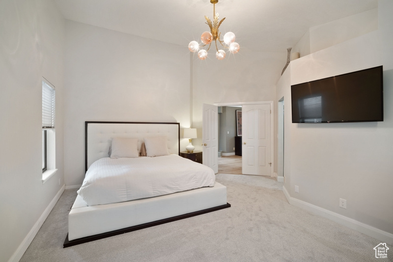 Carpeted bedroom with high vaulted ceiling, baseboards, and a notable chandelier