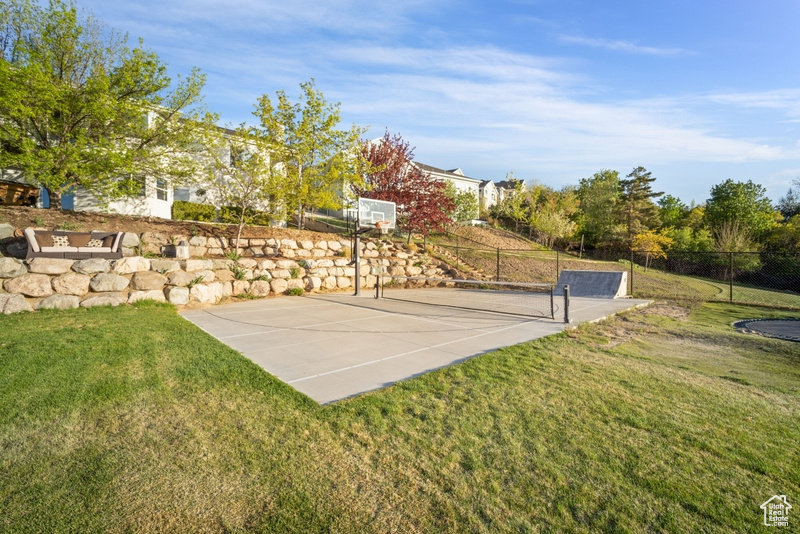 View of basketball court with a lawn, fence, and basketball hoop