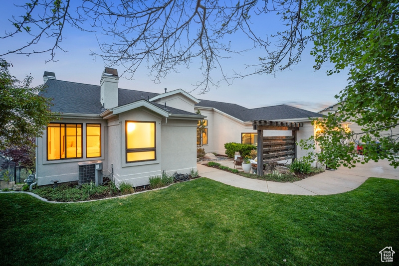 Exterior space with a pergola, stucco siding, a chimney, cooling unit, and a lawn