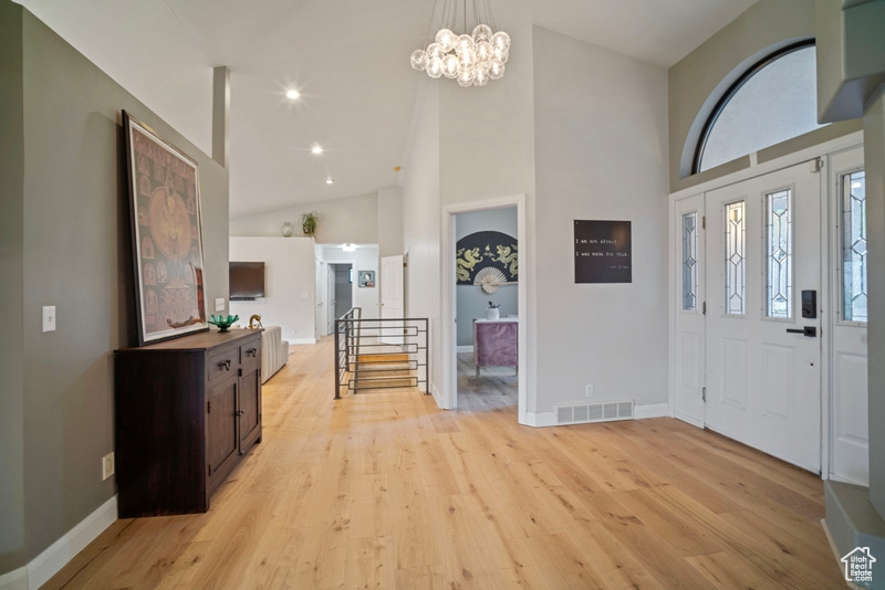 Entryway featuring visible vents, high vaulted ceiling, baseboards, light wood finished floors, and a chandelier