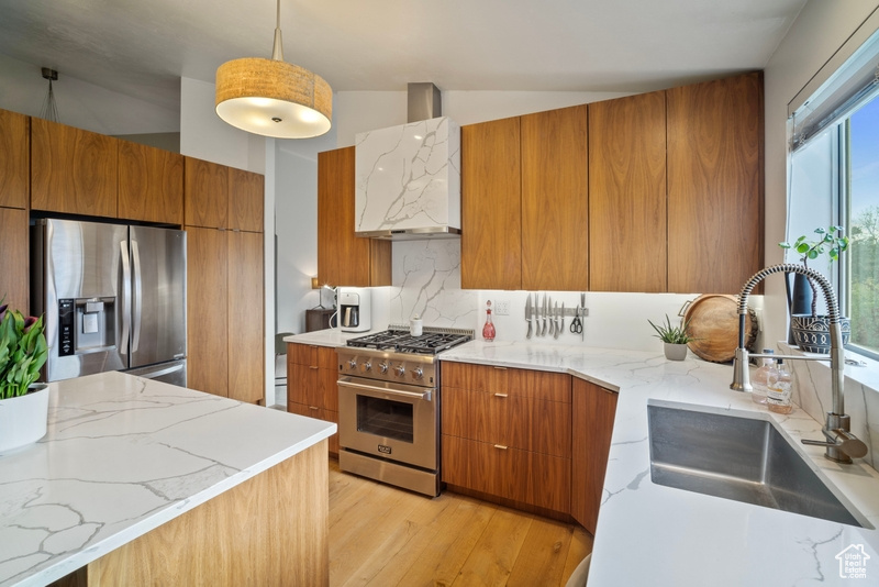 Kitchen featuring brown cabinetry, modern cabinets, wall chimney range hood, a sink, and appliances with stainless steel finishes