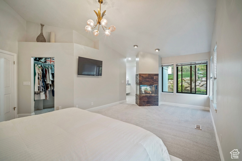 Carpeted bedroom with visible vents, a fireplace, baseboards, a chandelier, and lofted ceiling