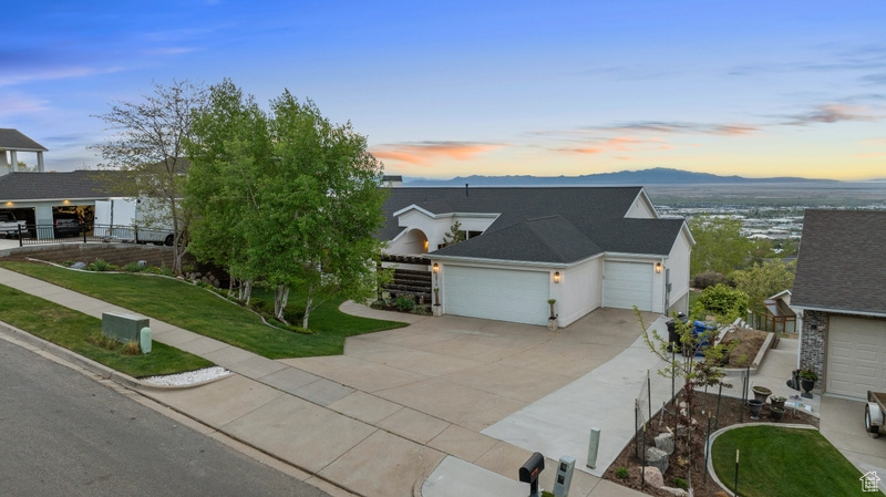 View of front of property featuring a mountain view, an attached garage, concrete driveway, and a front lawn