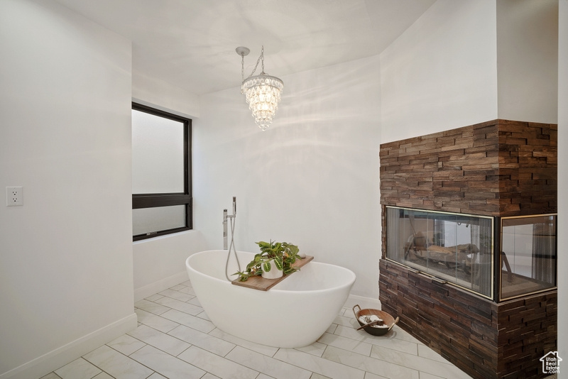Bathroom with a fireplace, baseboards, tile patterned floors, a freestanding bath, and a chandelier