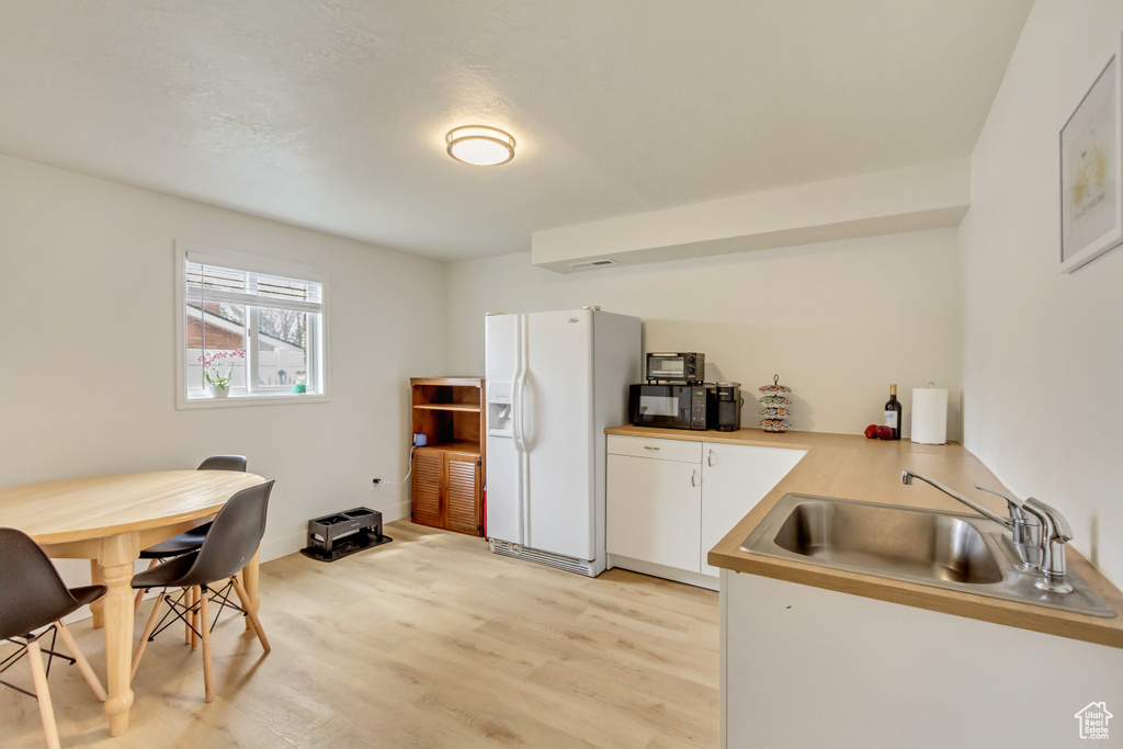 Kitchen with white cabinets, a sink, white refrigerator with ice dispenser, light wood-style floors, and light countertops