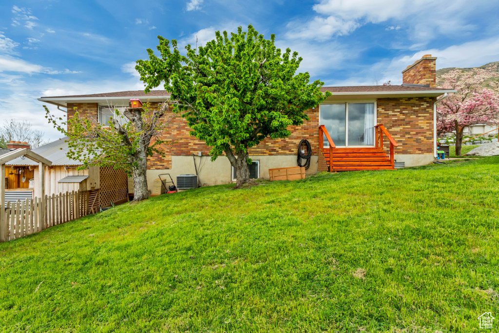 Rear view of property with a lawn, fence, a chimney, and central AC unit