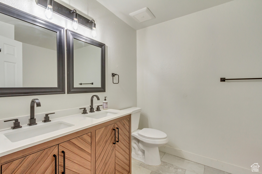 Bathroom with double vanity, toilet, baseboards, and a sink